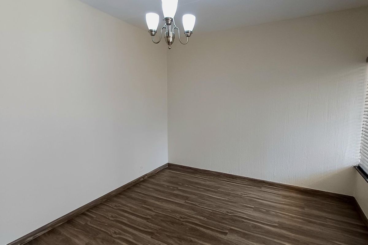 A clean, empty bedroom featuring modern laminate flooring, neutral walls, and fitted venetian blinds, ready for personalization.