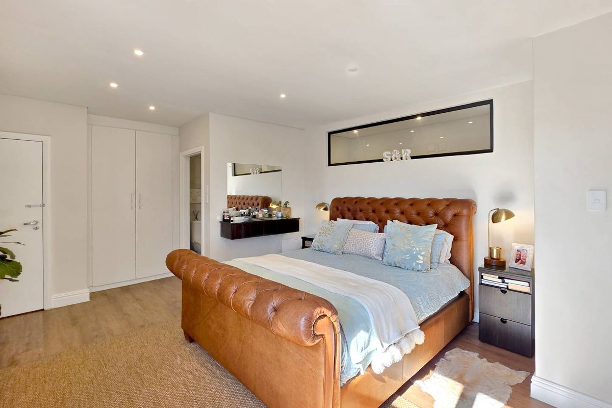 A well-maintained bedroom featuring laminate flooring, recessed downlighting, and built-in cupboards, with a unique high-level horizontal window providing additional natural light.