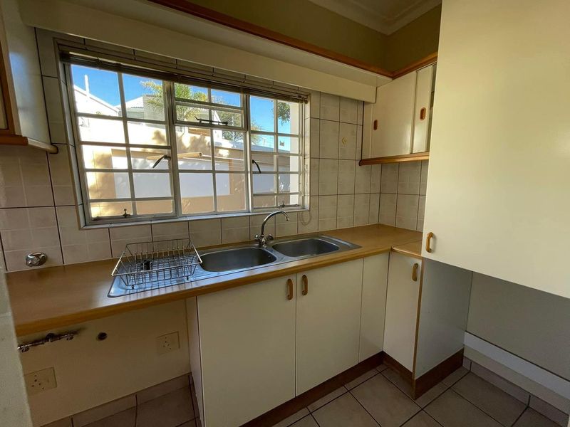 A functional kitchen area featuring a double basin sink, laminate countertops, tiled splashbacks, and ample built-in cabinetry, ready for a modern update.