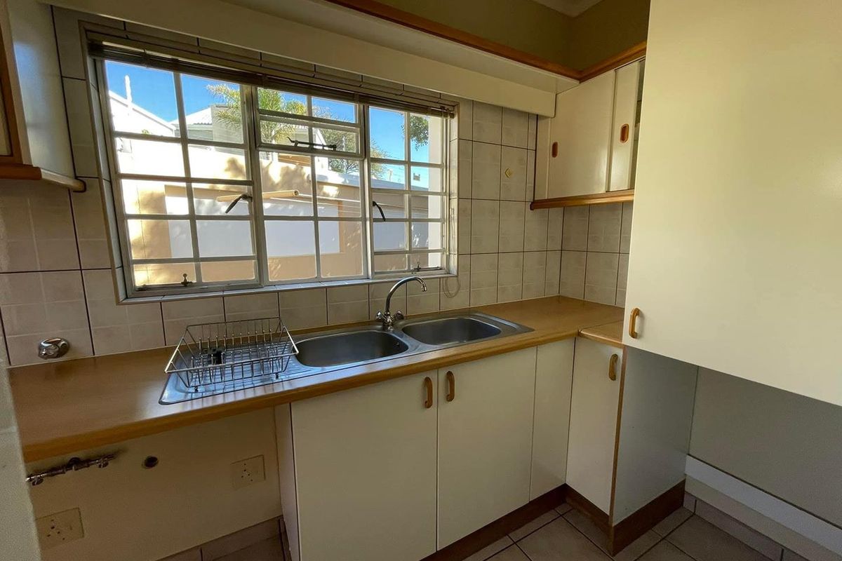A functional kitchen area featuring a double basin sink, laminate countertops, tiled splashbacks, and ample built-in cabinetry, ready for a modern update.