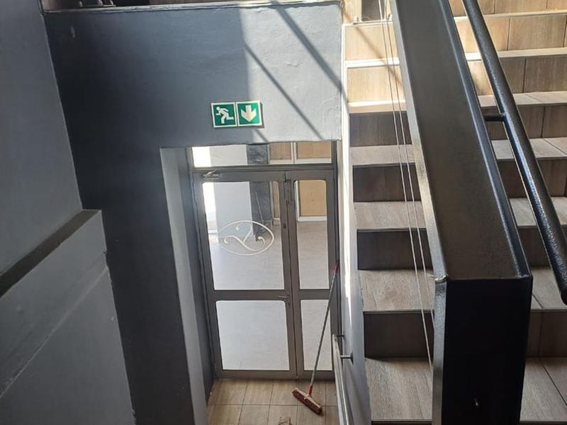A modern interior staircase featuring tiled steps, a sleek metal handrail with cable balustrade, and a glass door leading to an exit.