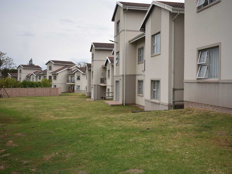 A view of the rear elevation of the apartment complex, featuring multi-story residential units with tiled roofs and a shared communal garden area.