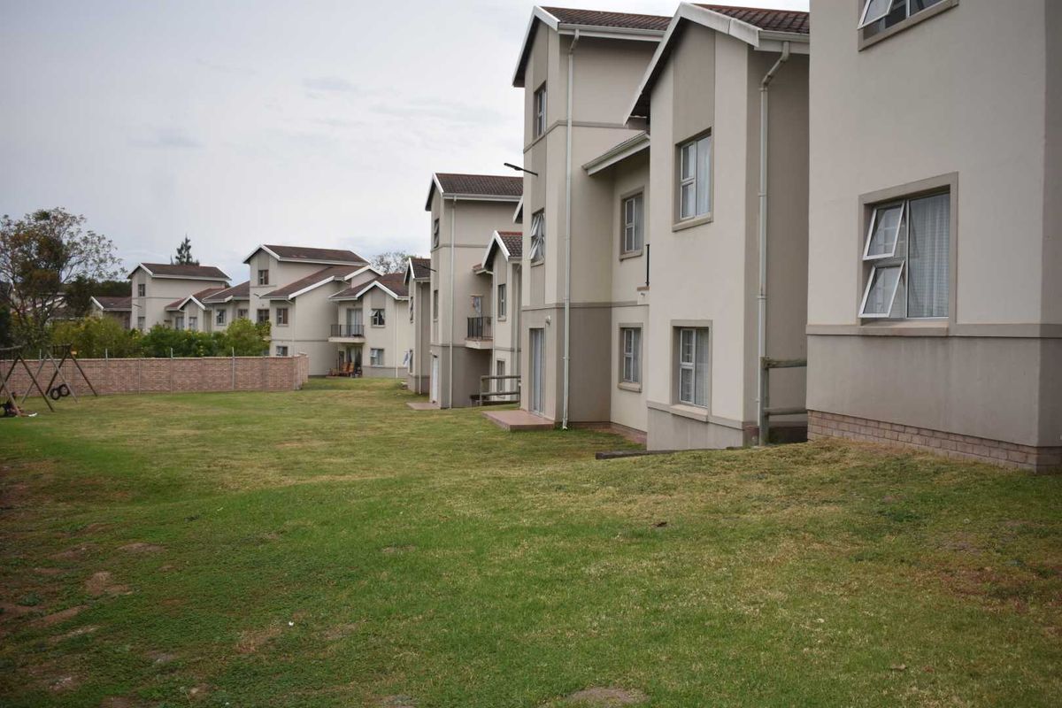 A view of the rear elevation of the apartment complex, featuring multi-story residential units with tiled roofs and a shared communal garden area.