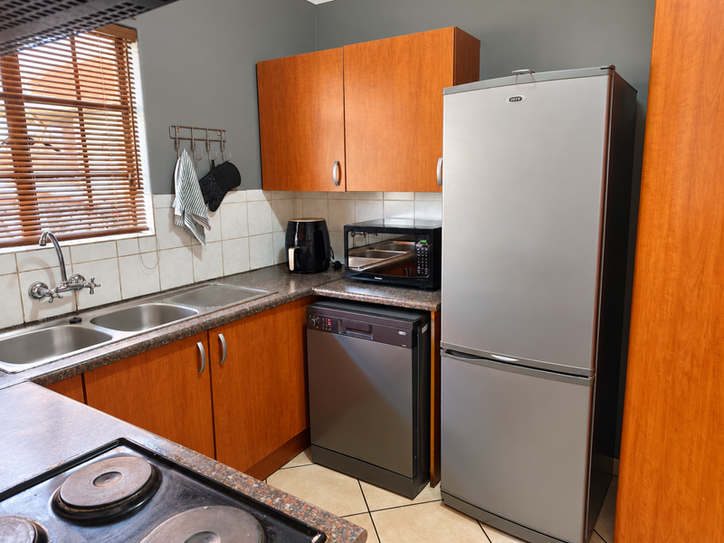Functional kitchen featuring laminate cabinetry, double sink, tiled backsplash, and built-in electric hob with integrated dishwasher space.
