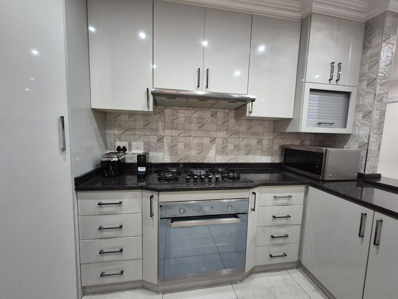 Modern kitchen featuring high-gloss cabinetry, granite countertops, a built-in gas hob, oven, and extractor fan with a stylish tiled backsplash.
