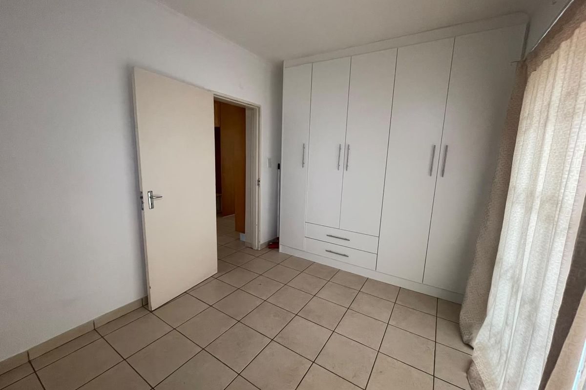 A bright, empty bedroom featuring neutral tiled flooring and a large, white built-in wardrobe with ample storage space.