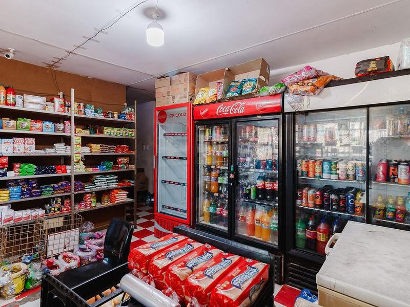 A utility space or storage area featuring commercial refrigeration units, extensive built-in shelving, and tiled flooring, currently utilized for retail inventory storage.
