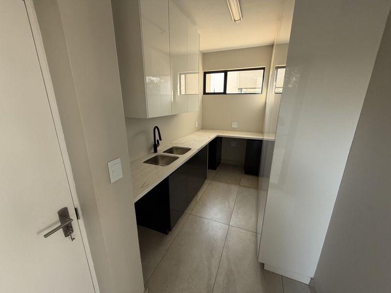 A modern, clean scullery featuring sleek black and white cabinetry, stone countertops, a double sink with a black mixer tap, and neutral floor tiles.