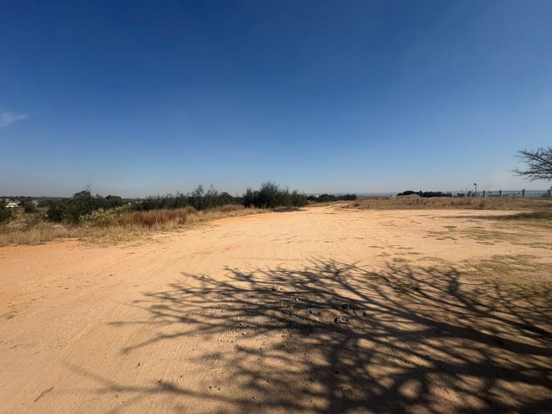 An expansive, undeveloped plot of land featuring natural ground cover and surrounding vegetation under a clear sky.