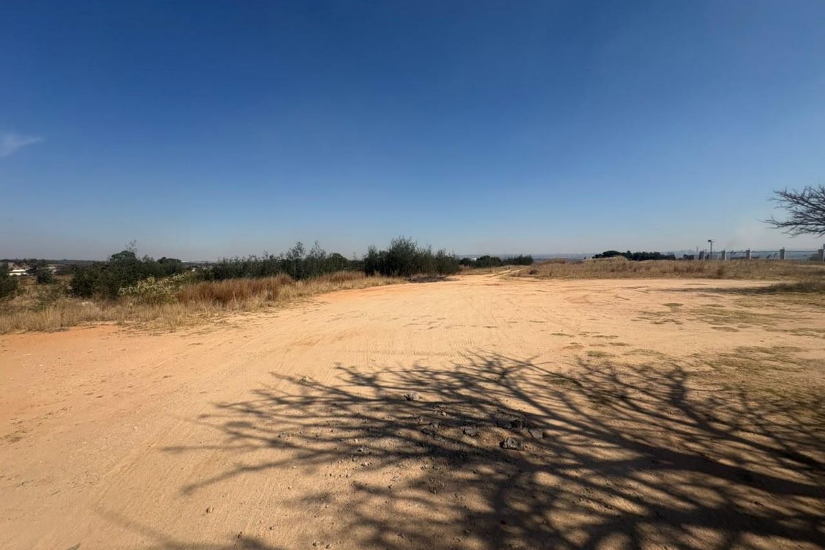 An expansive, undeveloped plot of land featuring natural ground cover and surrounding vegetation under a clear sky.
