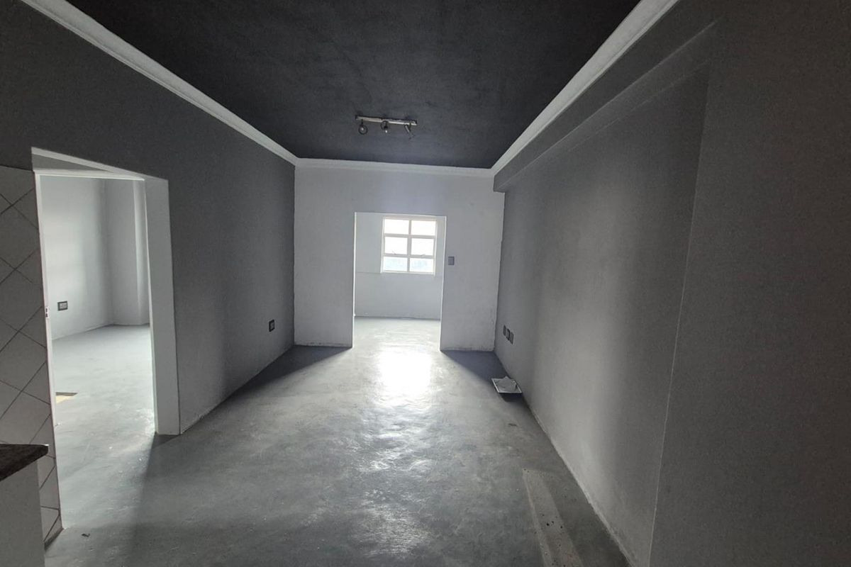 An empty living area featuring dark painted ceilings, crown molding, and concrete flooring, offering a blank canvas for interior design.