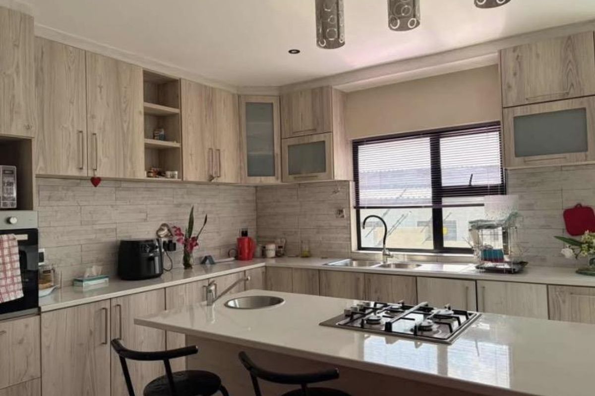 Modern kitchen featuring light wood-grain cabinetry, stone countertops, a central island with a gas hob, and integrated appliances.