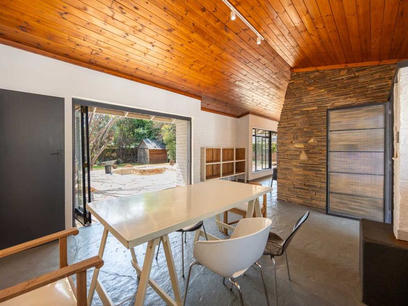 Spacious living area featuring a striking timber-clad vaulted ceiling, stone feature wall, and seamless indoor-outdoor flow through large bi-fold doors to the garden.