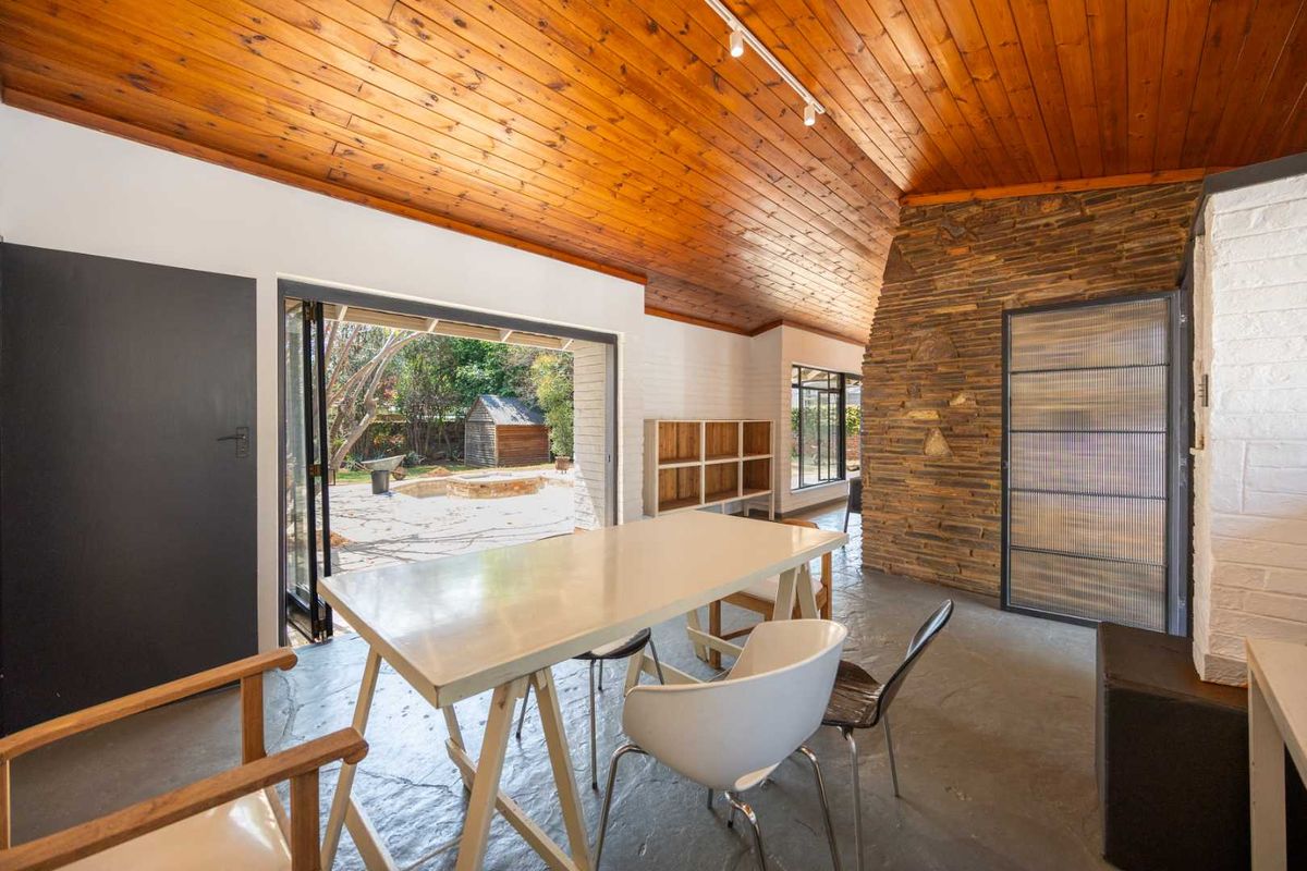Spacious living area featuring a striking timber-clad vaulted ceiling, stone feature wall, and seamless indoor-outdoor flow through large bi-fold doors to the garden.