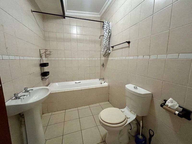 A functional bathroom featuring a pedestal basin, built-in bathtub, and toilet with neutral wall and floor tiling.
