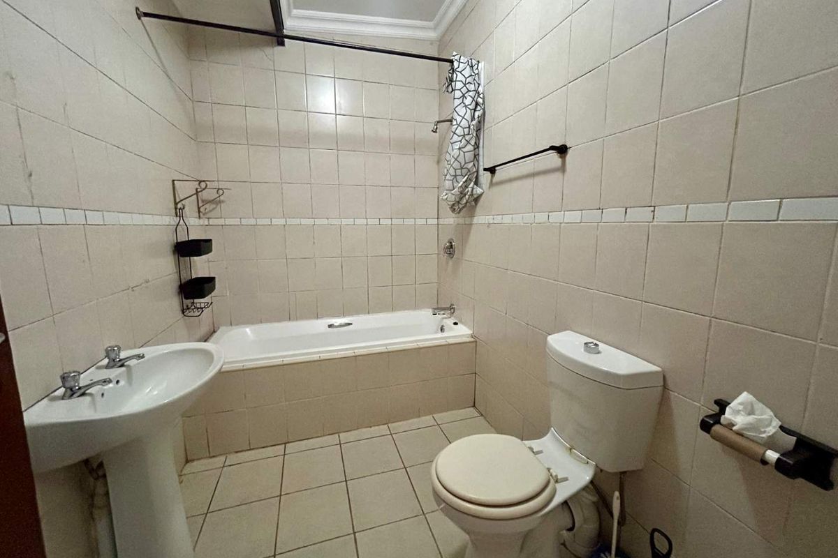 A functional bathroom featuring a pedestal basin, built-in bathtub, and toilet with neutral wall and floor tiling.