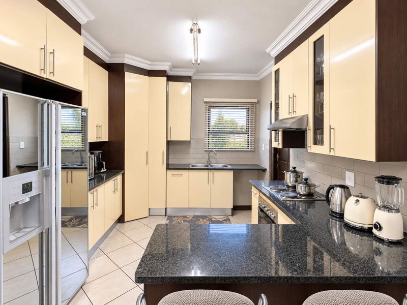 A well-maintained kitchen featuring granite countertops, ample built-in cabinetry, a stainless steel extractor fan, and a functional layout with tiled flooring.