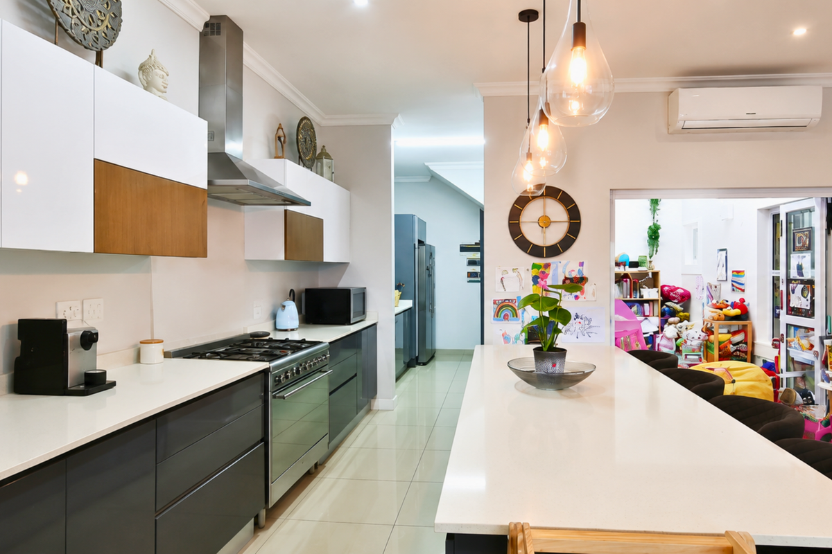 Modern kitchen featuring a large central island, quartz countertops, gas stove with extractor fan, and sleek two-tone cabinetry, flowing into an adjacent living area.