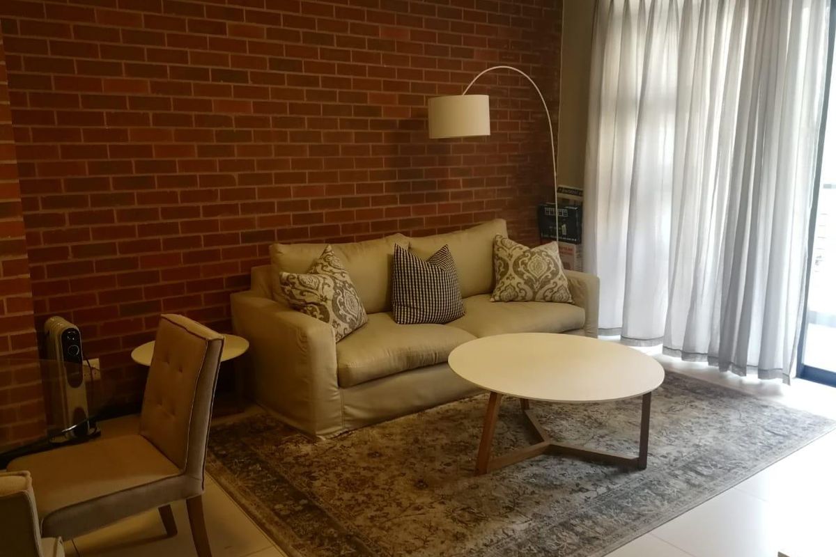 A living room featuring an exposed brick feature wall, tiled flooring, and access to an outdoor area through a sliding glass door.
