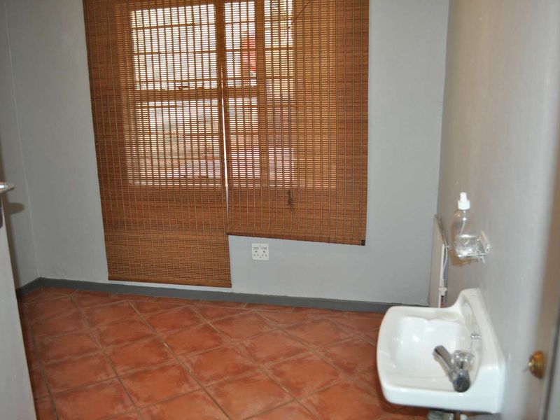 A simple, empty bathroom featuring tiled flooring and a wall-mounted basin, offering a blank canvas for potential renovation or modernization.