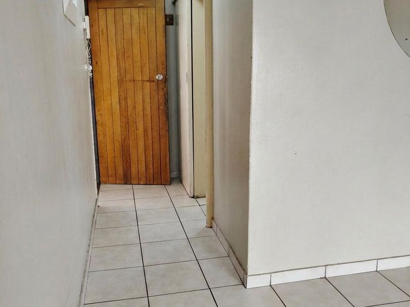A functional hallway featuring tiled flooring, a wooden door, and a sliding door, providing access to other areas of the apartment.