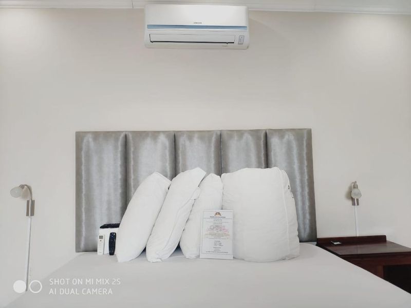 A bedroom featuring a neutral upholstered headboard, wall-mounted reading lights, and a split-system air conditioning unit.