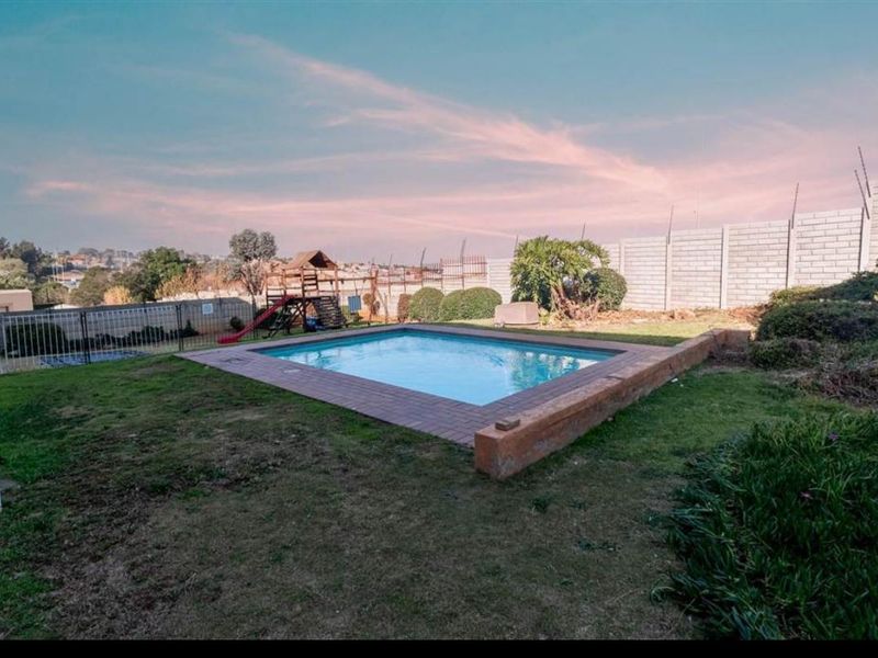 Outdoor pool area featuring a swimming pool with brick coping, surrounded by a lawn and secured by a perimeter wall with electric fencing.