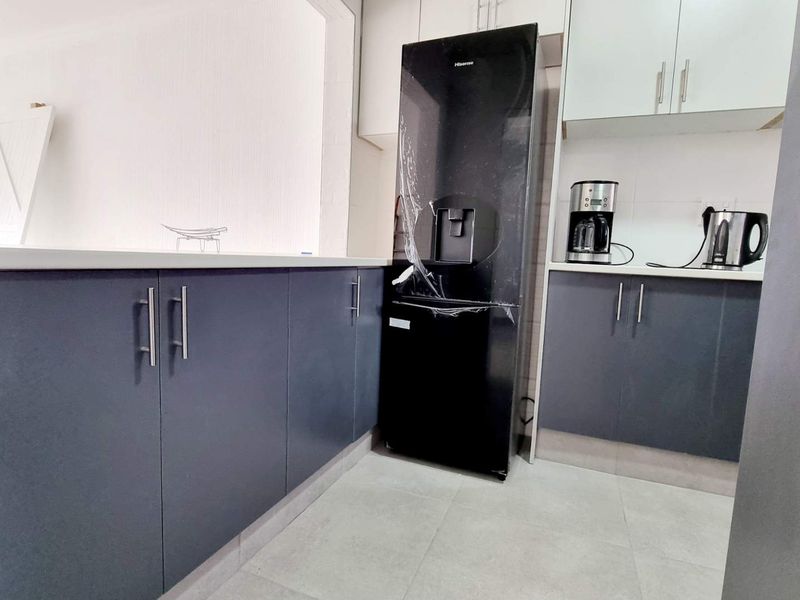 Modern kitchen featuring dark grey lower cabinetry, white upper cabinets, stone countertops, and tiled flooring, currently undergoing final finishing touches.