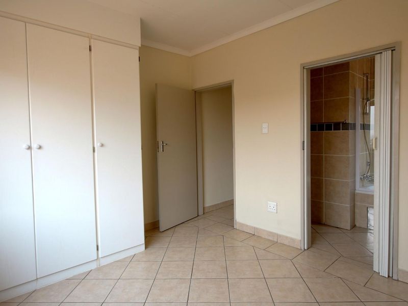 A clean, empty bedroom featuring tiled flooring, built-in cupboards, and direct access to an en-suite bathroom.