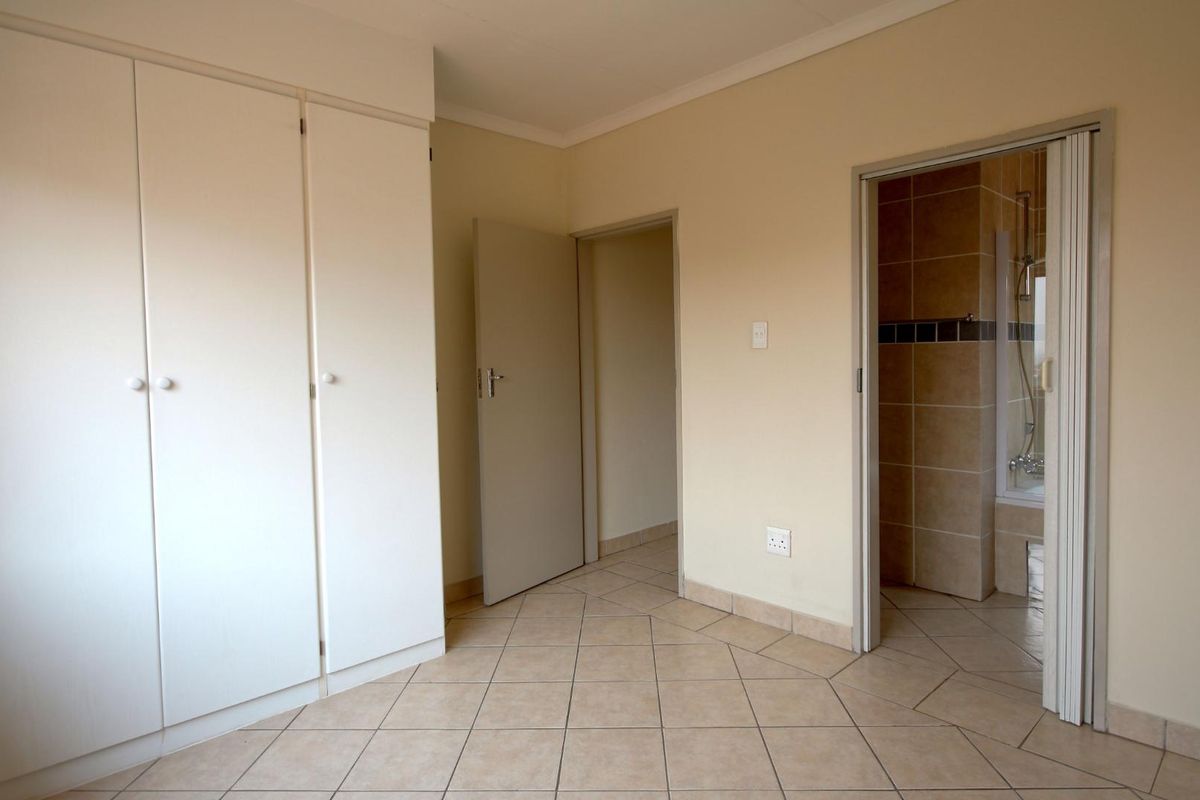 A clean, empty bedroom featuring tiled flooring, built-in cupboards, and direct access to an en-suite bathroom.