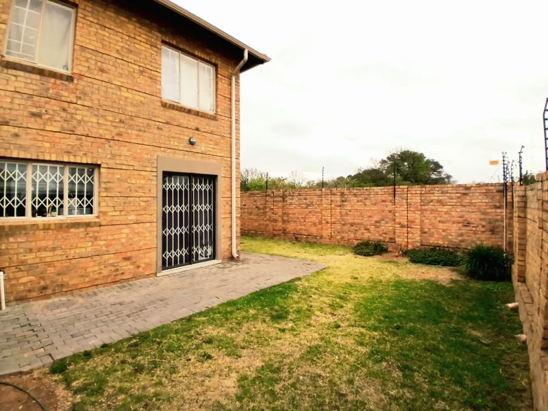 Rear view of a face brick townhouse featuring a paved patio area, enclosed garden with perimeter walling, and security features on windows and doors.