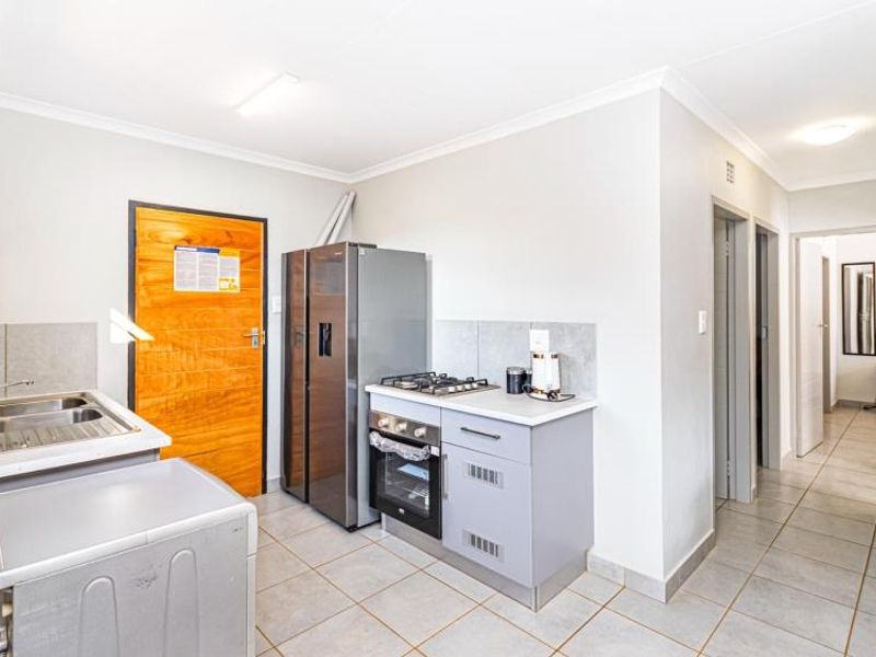 Compact kitchen featuring fitted cabinetry, a gas hob, built-in oven, stainless steel sink, and tiled flooring, leading into a hallway.