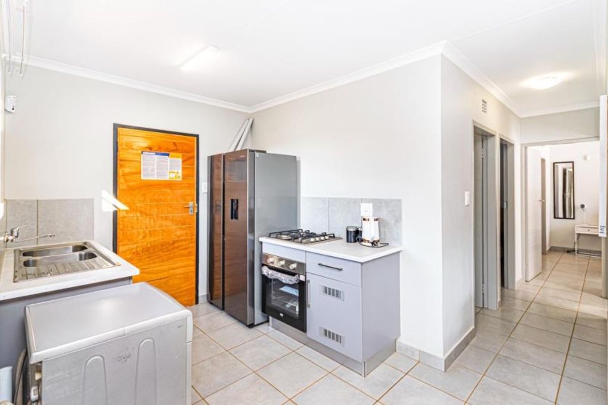 Compact kitchen featuring fitted cabinetry, a gas hob, built-in oven, stainless steel sink, and tiled flooring, leading into a hallway.