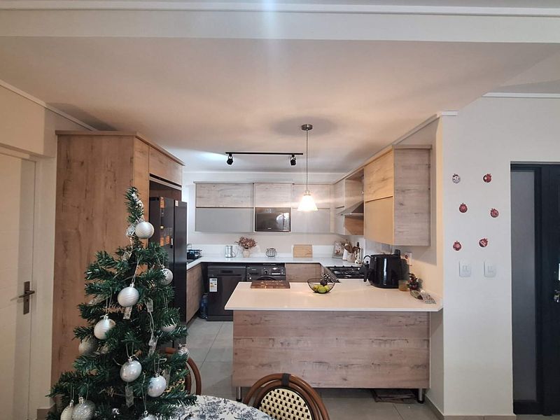 Modern kitchen featuring wood-grain cabinetry, stone countertops, integrated appliances, and a functional breakfast bar layout with contemporary lighting.