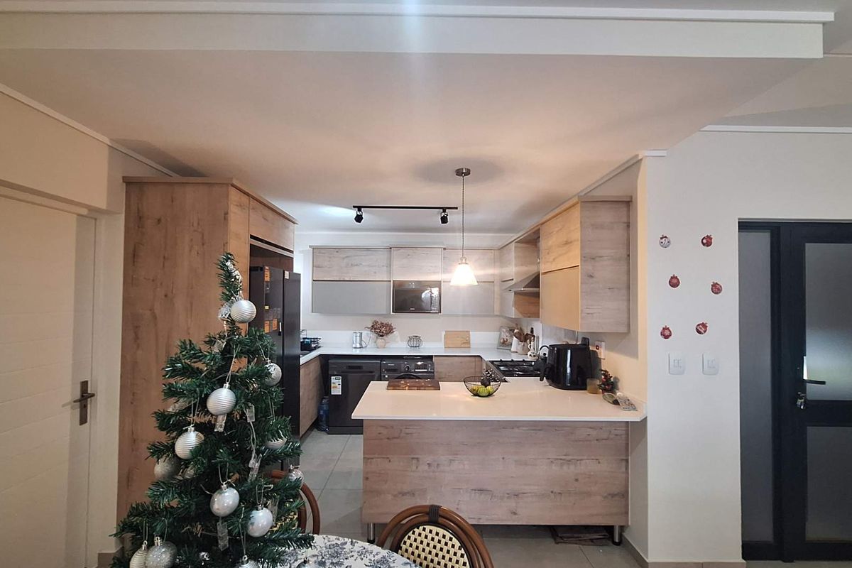 Modern kitchen featuring wood-grain cabinetry, stone countertops, integrated appliances, and a functional breakfast bar layout with contemporary lighting.