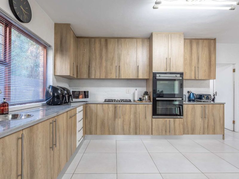 A functional kitchen featuring wood-look cabinetry, a built-in double oven, gas hob, and tiled flooring with ample counter space.