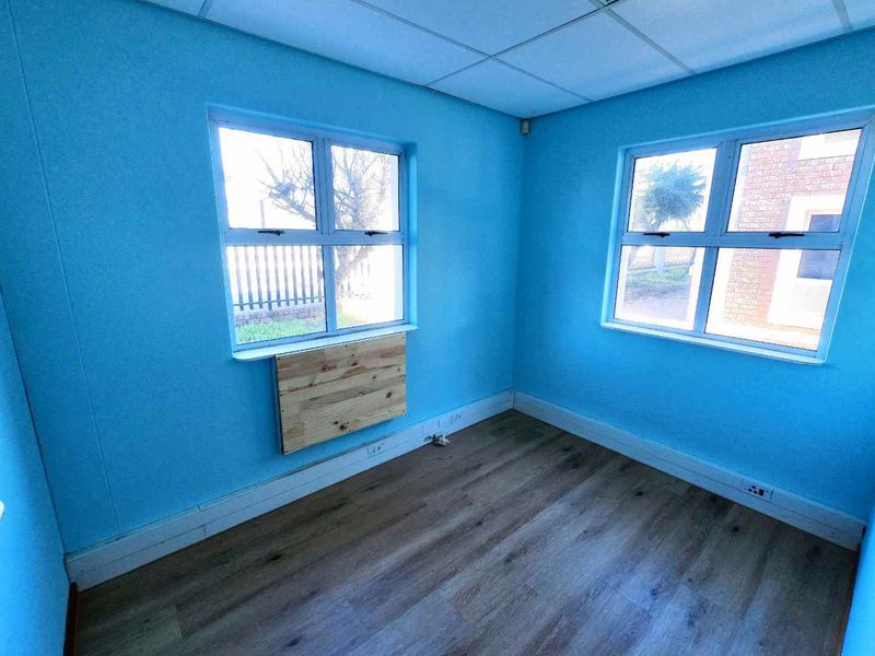 A vacant office space featuring blue walls, laminate flooring, and a suspended ceiling, offering a blank canvas for professional customization.