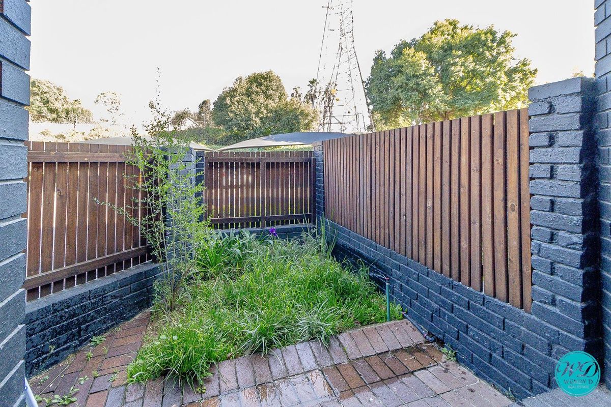 A private rear courtyard featuring a paved patio area, enclosed by painted brick walls and timber slat fencing.
