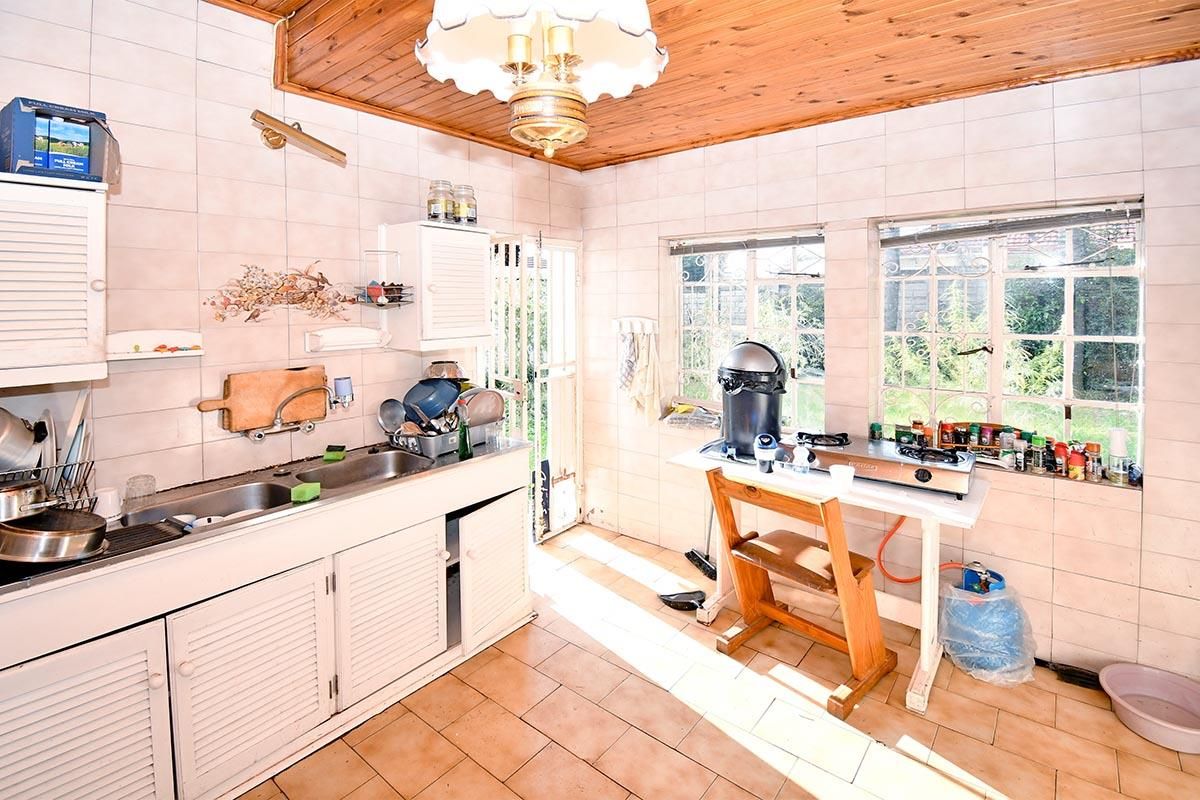 A dated kitchen featuring tiled walls, timber ceiling, double sink, and large windows providing natural light and garden views.