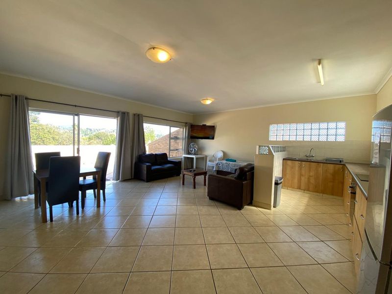 Spacious open-plan living and kitchen area featuring tiled flooring, large sliding doors for natural light, and functional kitchen cabinetry with integrated appliances.