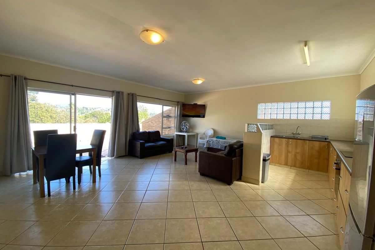 Spacious open-plan living and kitchen area featuring tiled flooring, large sliding doors for natural light, and functional kitchen cabinetry with integrated appliances.