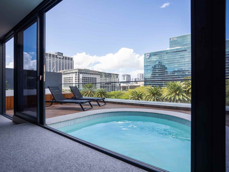 A private balcony featuring a plunge pool, timber decking, and a glass balustrade with expansive city skyline views.