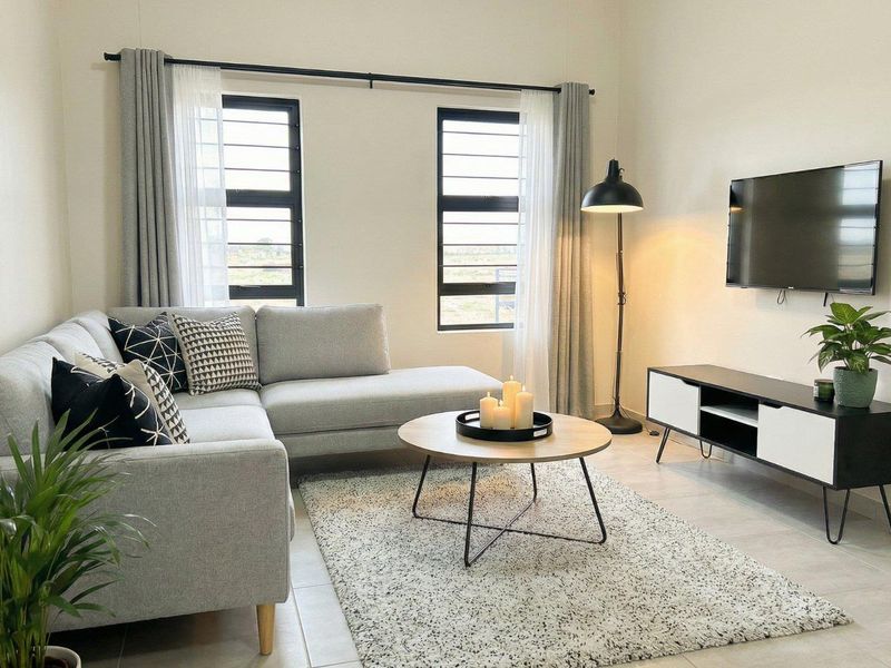 A bright and modern living room featuring neutral tiled flooring and large aluminium-framed windows that provide ample natural light.