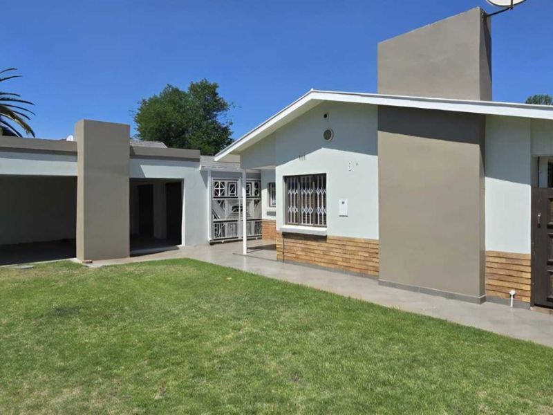 Front view of a single-story house featuring a carport, paved driveway, security gates, and a well-maintained lawn.