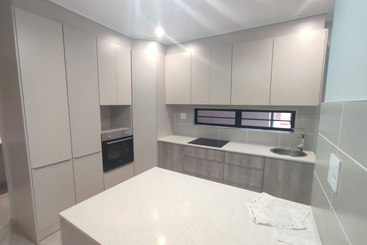 Modern kitchen featuring sleek handleless cabinetry, stone countertops, built-in oven, electric hob, and a functional island layout.