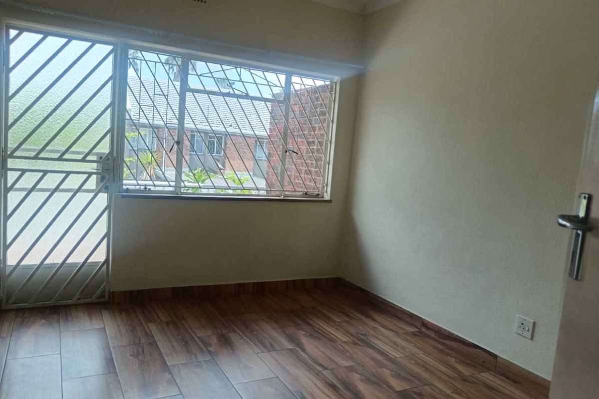 An empty bedroom featuring modern wood-look laminate flooring, a security gate, and burglar bars on the window for added safety.