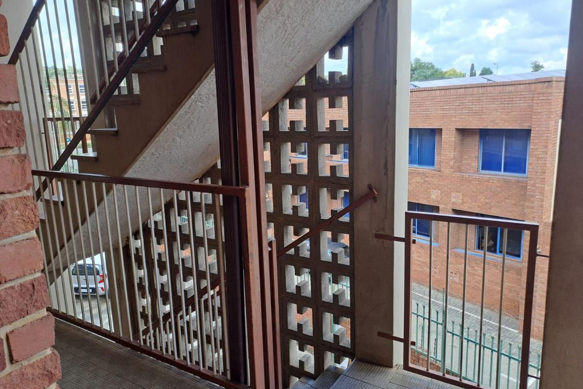 Exterior stairwell area featuring concrete stairs, metal safety railings, and decorative breeze block screening in an apartment complex setting.