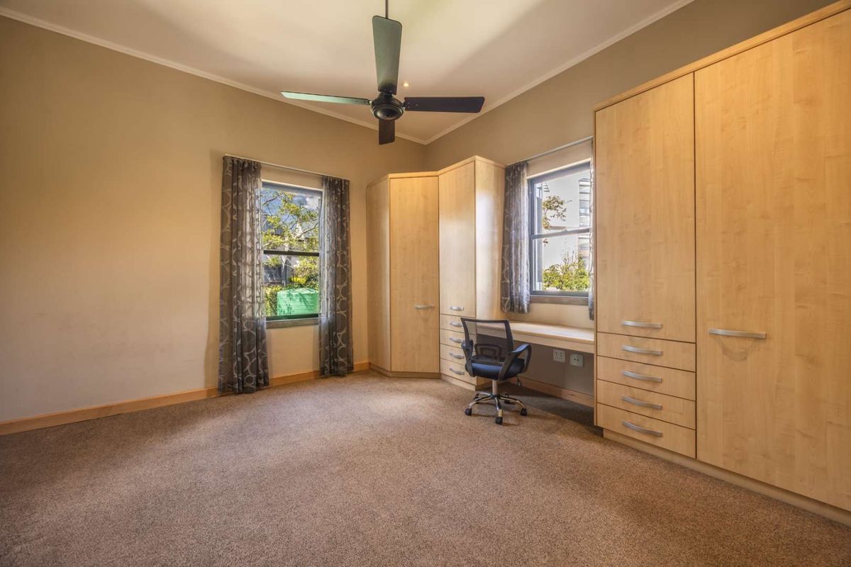Spacious bedroom featuring neutral walls, carpeted flooring, a ceiling fan, and extensive built-in cabinetry with an integrated desk area.