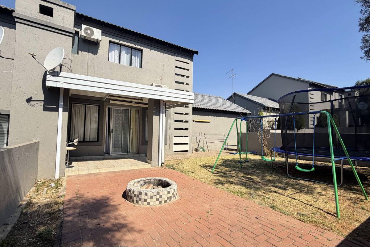 Rear view of the townhouse featuring a covered patio, brick-paved fire pit area, and a private garden space.