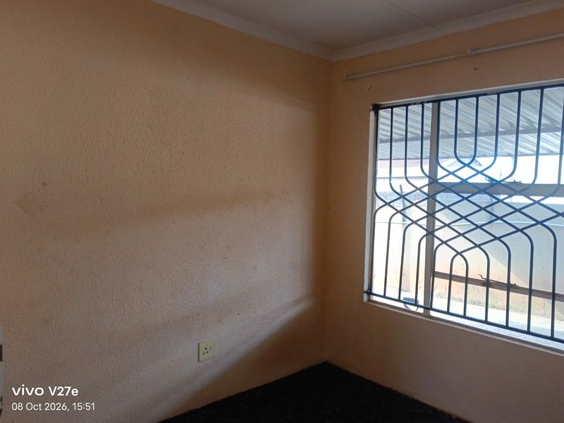 An empty bedroom featuring a window with a security gate and standard electrical outlets, requiring cosmetic updates to the wall finishes.